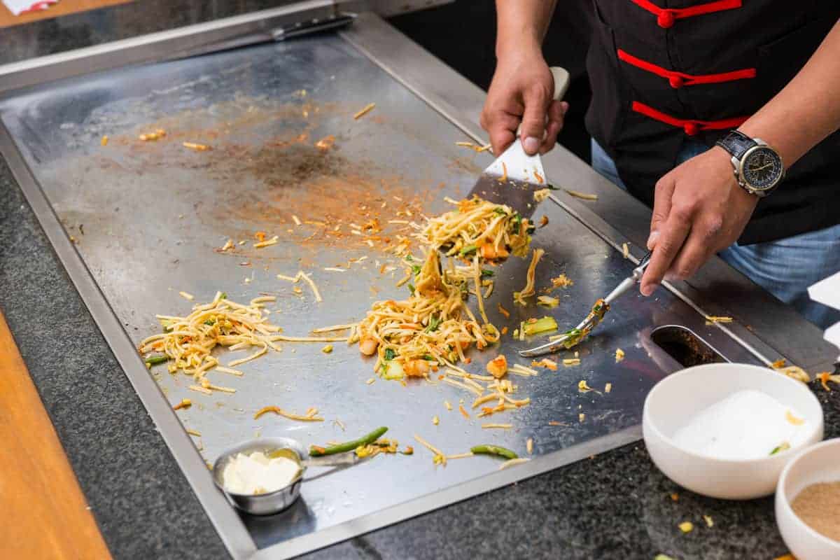 chef preparing asian noodles on flat top grill