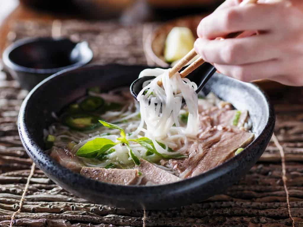 eating bowl of beef brisket pho with chopsticks and spoon