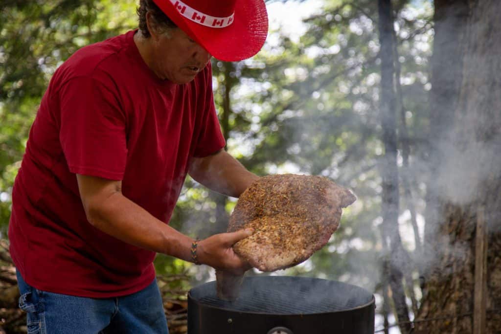 mans hands placing a large beef brisket on a smoker