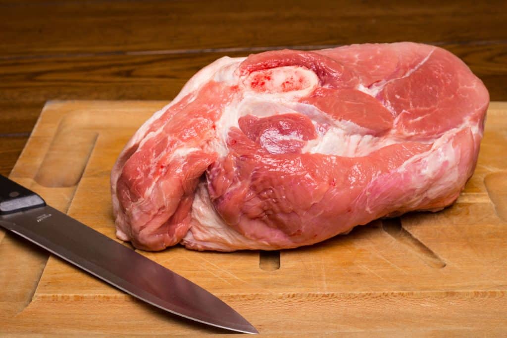 raw cut of pork shoulder on board with knife