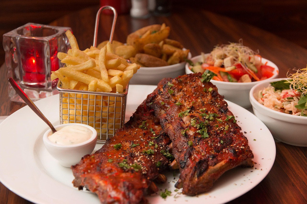 Baby back ribs and fries on a white plate.