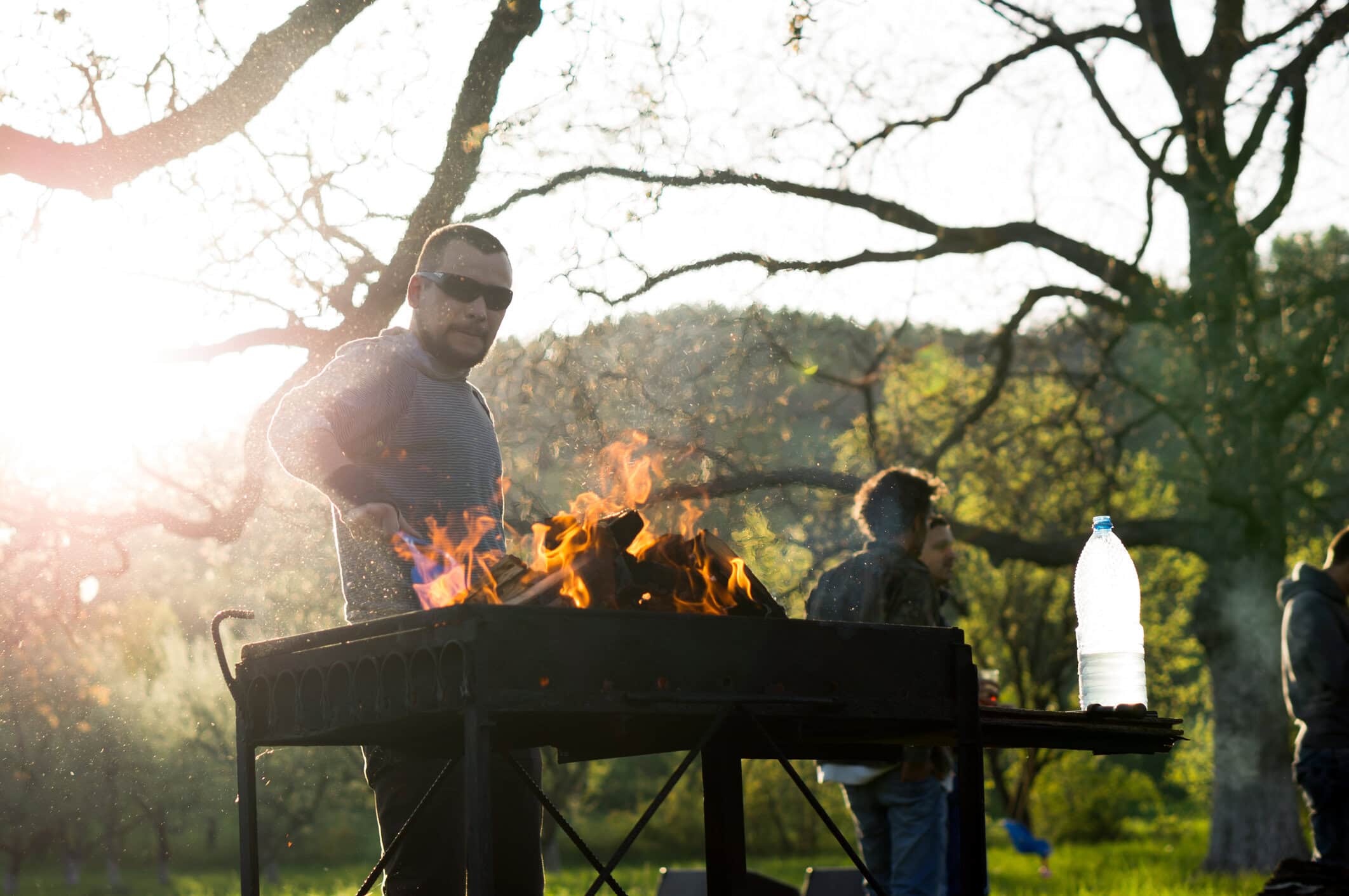 Person grilling raw beef burger patties over smoky charcoal flames on an outdoor barbecue grill.