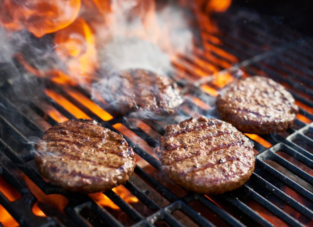 Juicy burgers cooking over fire on a hot barbecue grill.