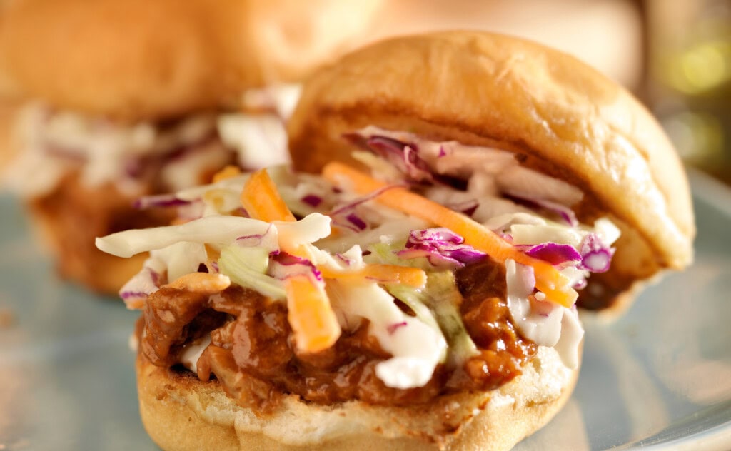 Close-up of a pulled pork sandwich topped with creamy coleslaw on a toasted bun, served on a blue plate.