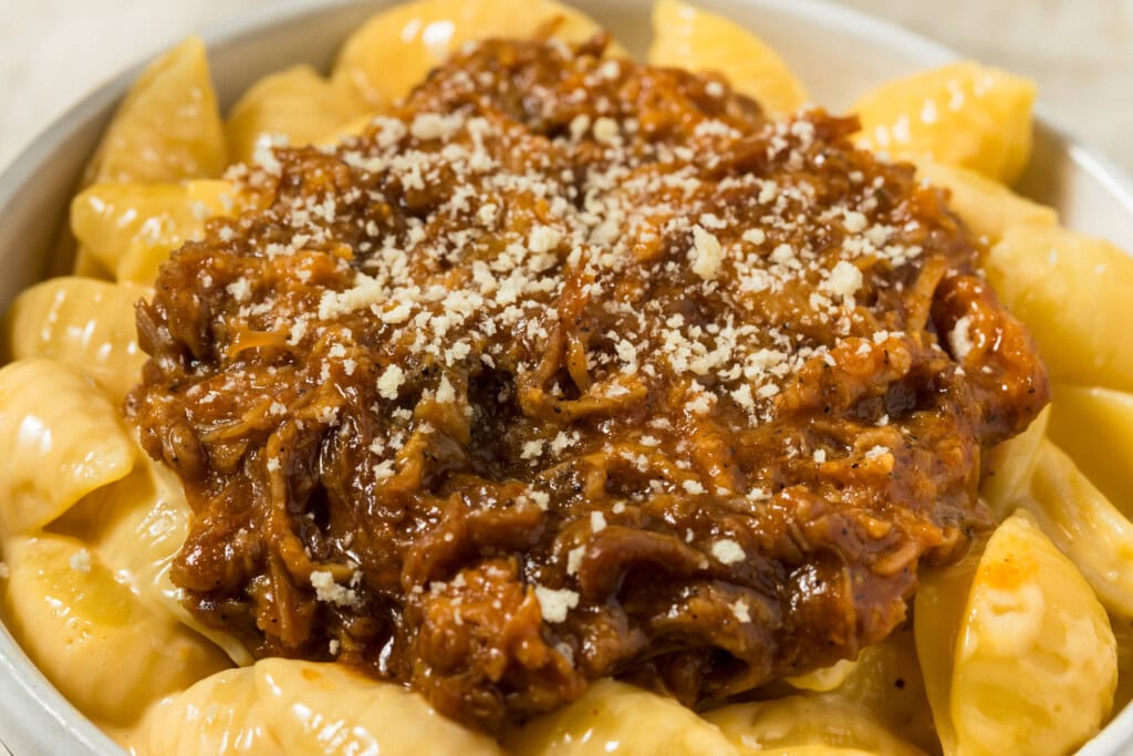 Bowl of creamy macaroni and cheese topped with pulled pork in barbecue sauce and sprinkled with breadcrumbs.